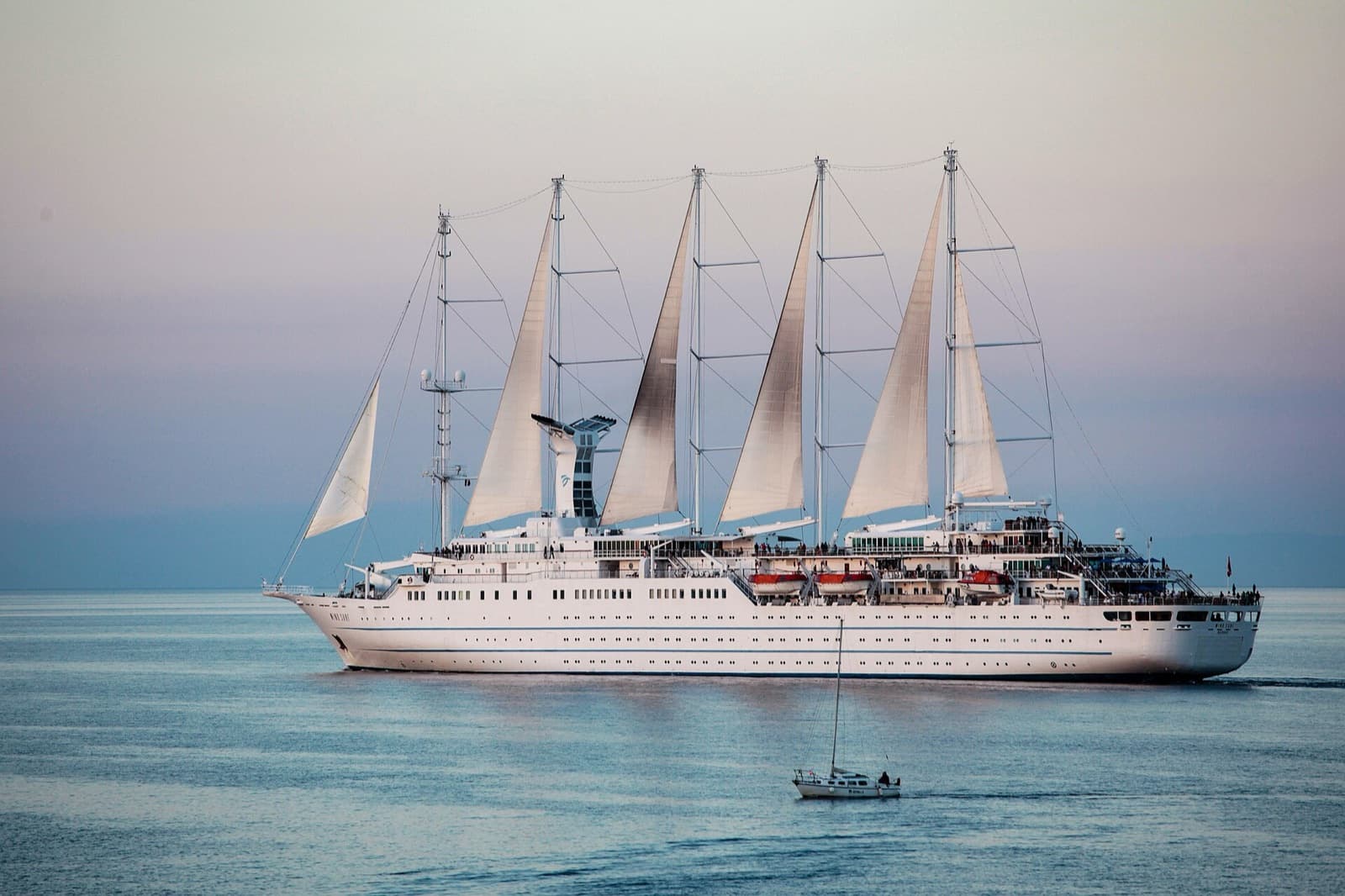 Windstar sailing cruise ship Wind Surf under sail on her five masts, leaving Cavo on the island of Elba at dusk