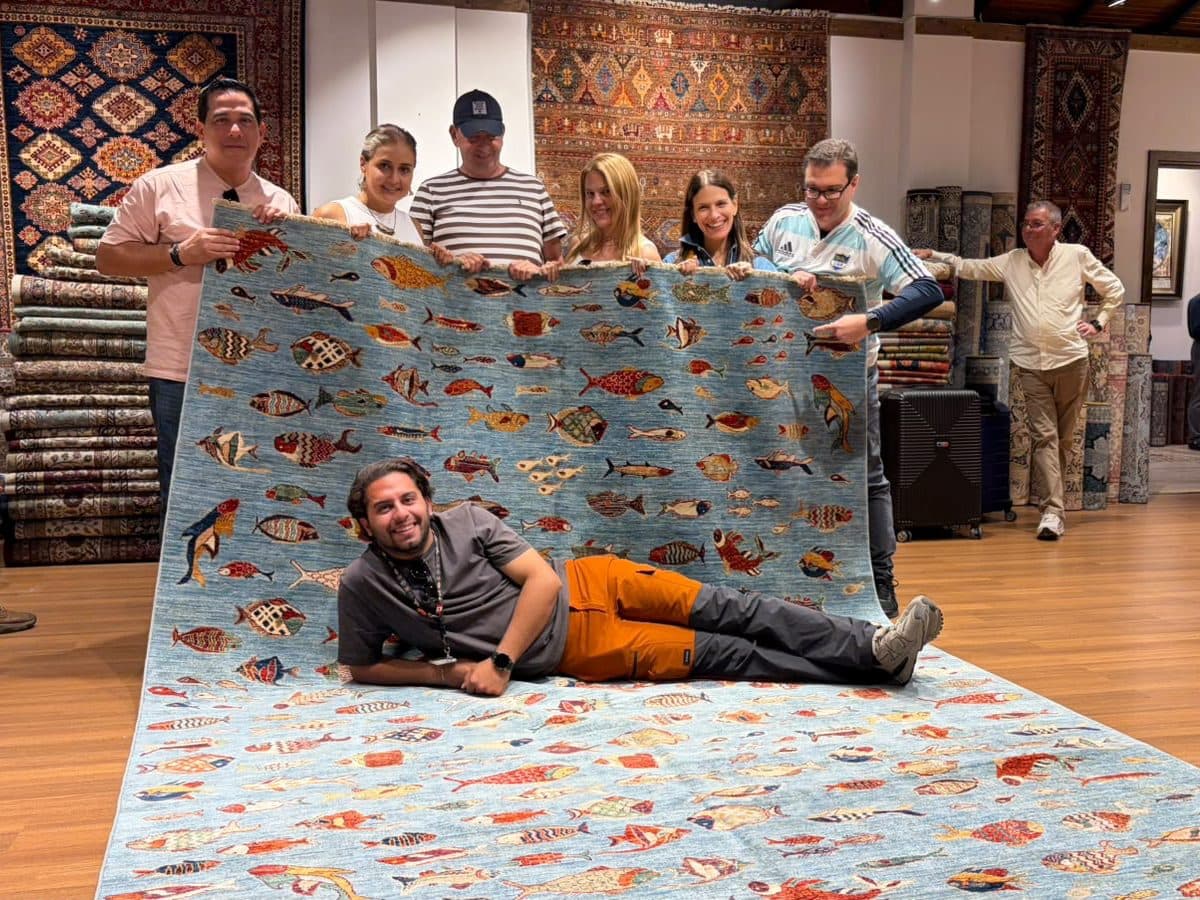 Six guests from Panama off Celebrity Ascent holding up a blue fish-pattern Turkish carpet at the Nakkaş Ephesus Handicraft Center, an optional stop they asked for on a private full-day Ephesus tour from Kuşadası cruise port with licensed guide Celal Ceylan, 22 October 2026