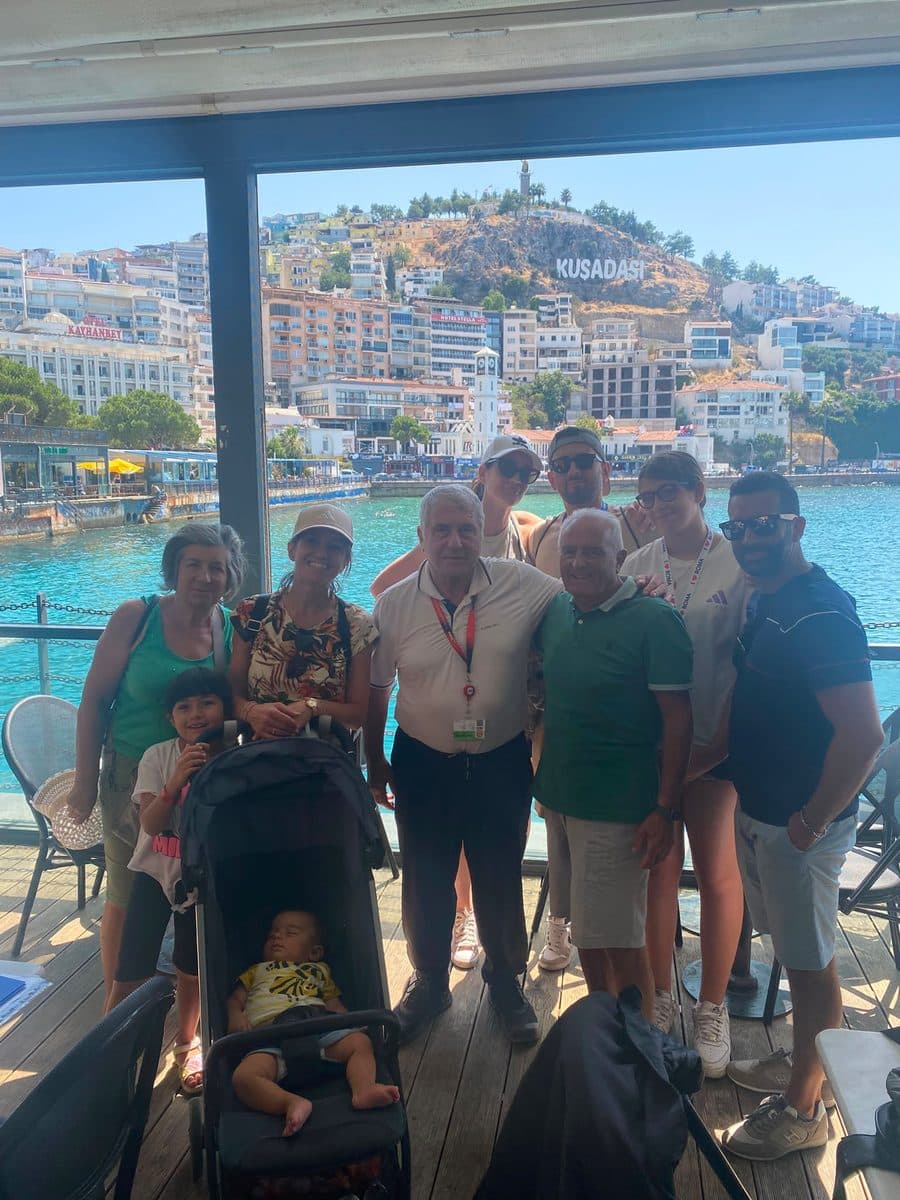 Celebrity Infinity guests meeting their licensed guide Nedret Güngör on the Starbucks terrace at Kuşadası cruise port, the KUŞADASI hillside sign behind them, 28 July 2026
