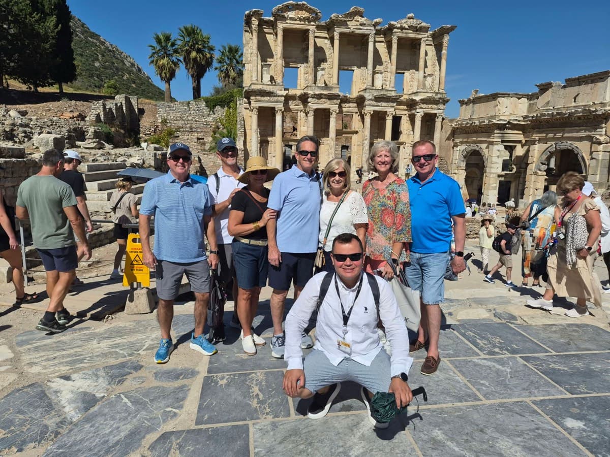 Tours of Ephesus guide Zafer Korkmaz kneeling in front of seven Celebrity Xcel guests before the Library of Celsus and the Gate of Augustus, Ephesus, 9 September 2026