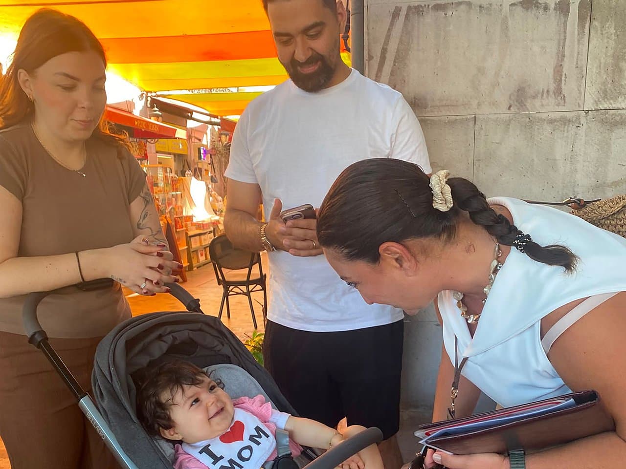 Tours of Ephesus guide Fulya Tamer welcoming a young family with a baby in a stroller at the Kuşadası cruise port plaza, tour papers in hand