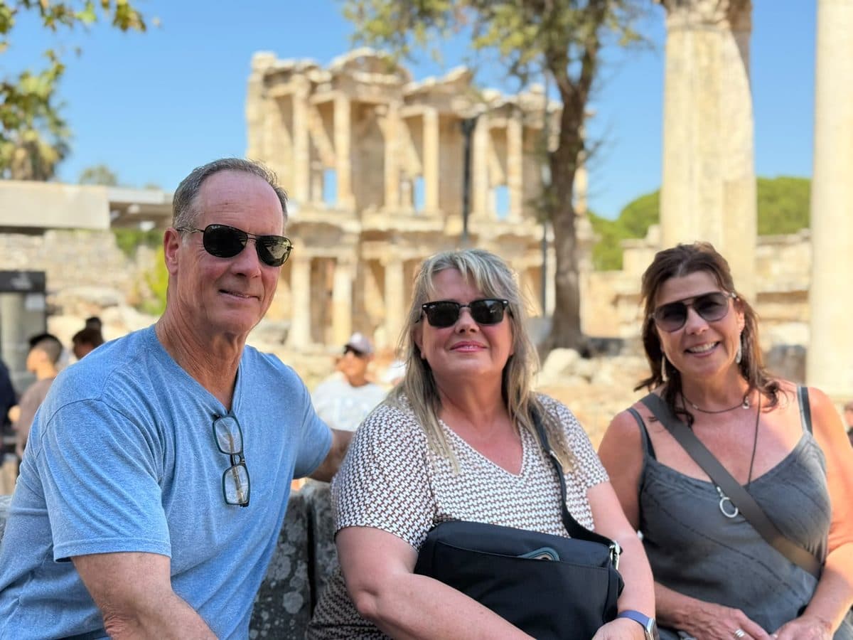 Three Oceania Nautica guests resting on ancient stones in front of the Library of Celsus on a private Ephesus tour from Kuşadası cruise port, photographed by their licensed guide Mehmet Tunalı, 24 September 2026