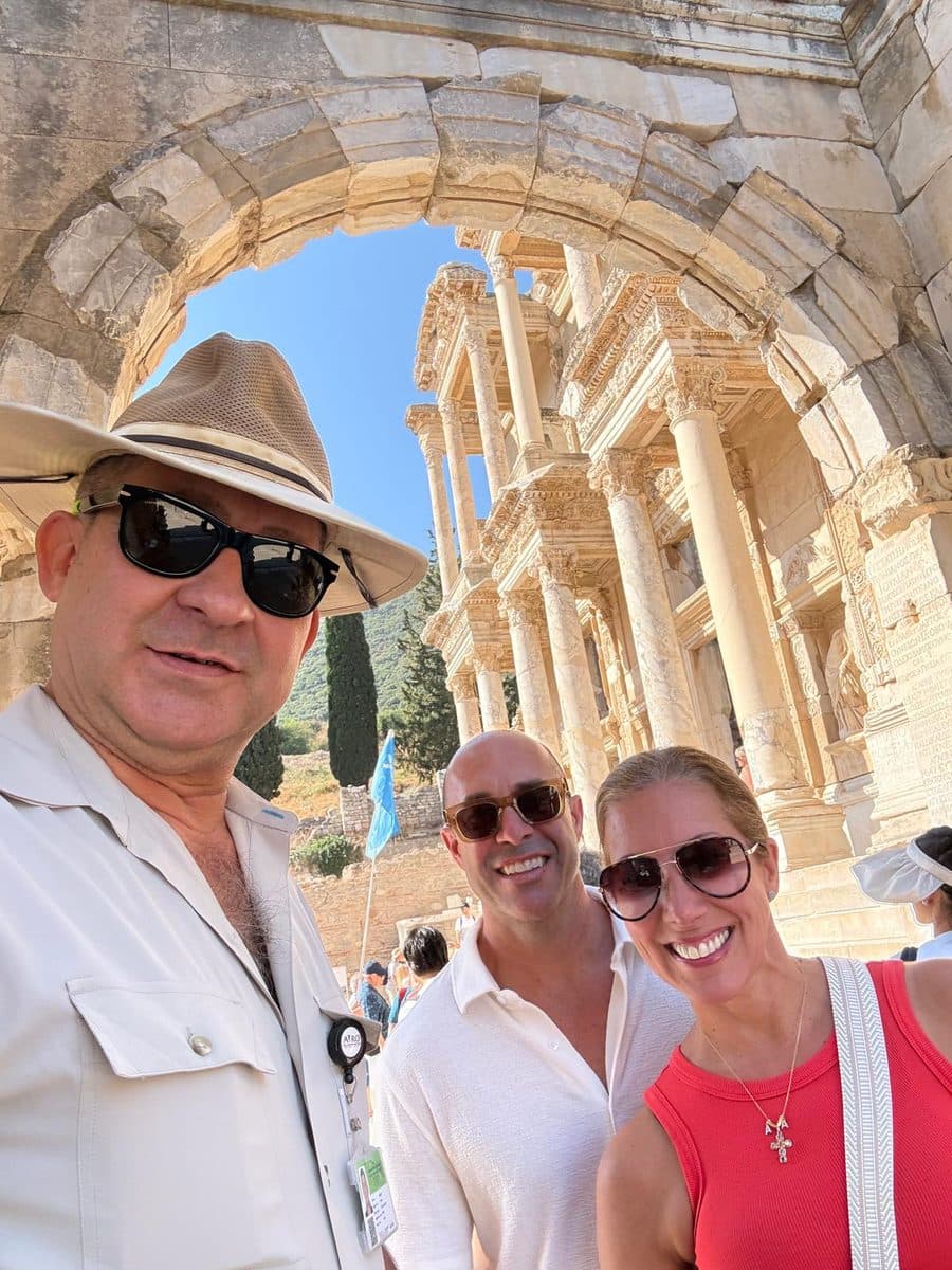 Licensed English- and Russian-speaking guide Mehmet Tunalı and two Ritz-Carlton Evrima guests beneath a stone arch that frames the Library of Celsus at Ephesus, on a private Ephesus tour in English from Kuşadası cruise port, 21 September 2026