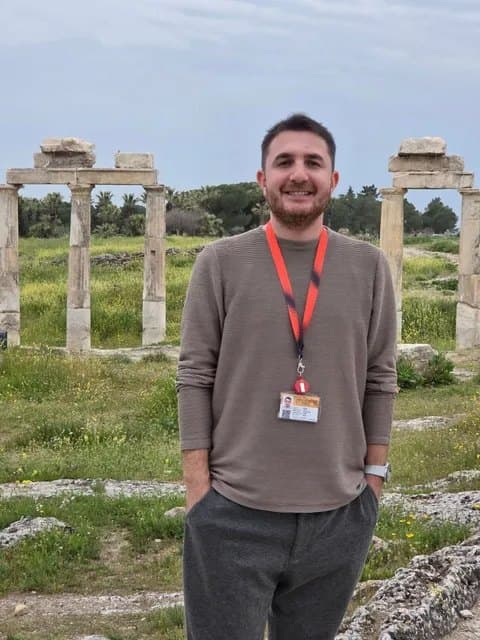 Cihan Ünlü, a licensed Tours of Ephesus guide who leads private tours from Kuşadası cruise port in Spanish and Portuguese, wearing his guide badge on a lanyard among the columns of an ancient site
