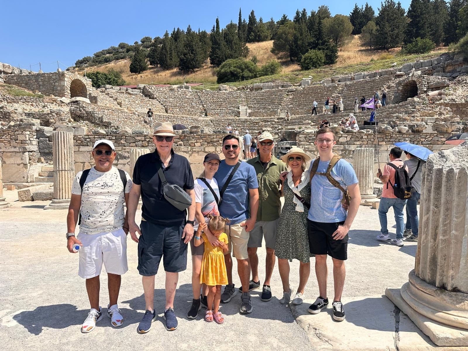 A Tours of Ephesus private guest group photographed at the foot of the Great Theatre of Ephesus, with the Roman tiers and surrounding pine-covered hills behind them