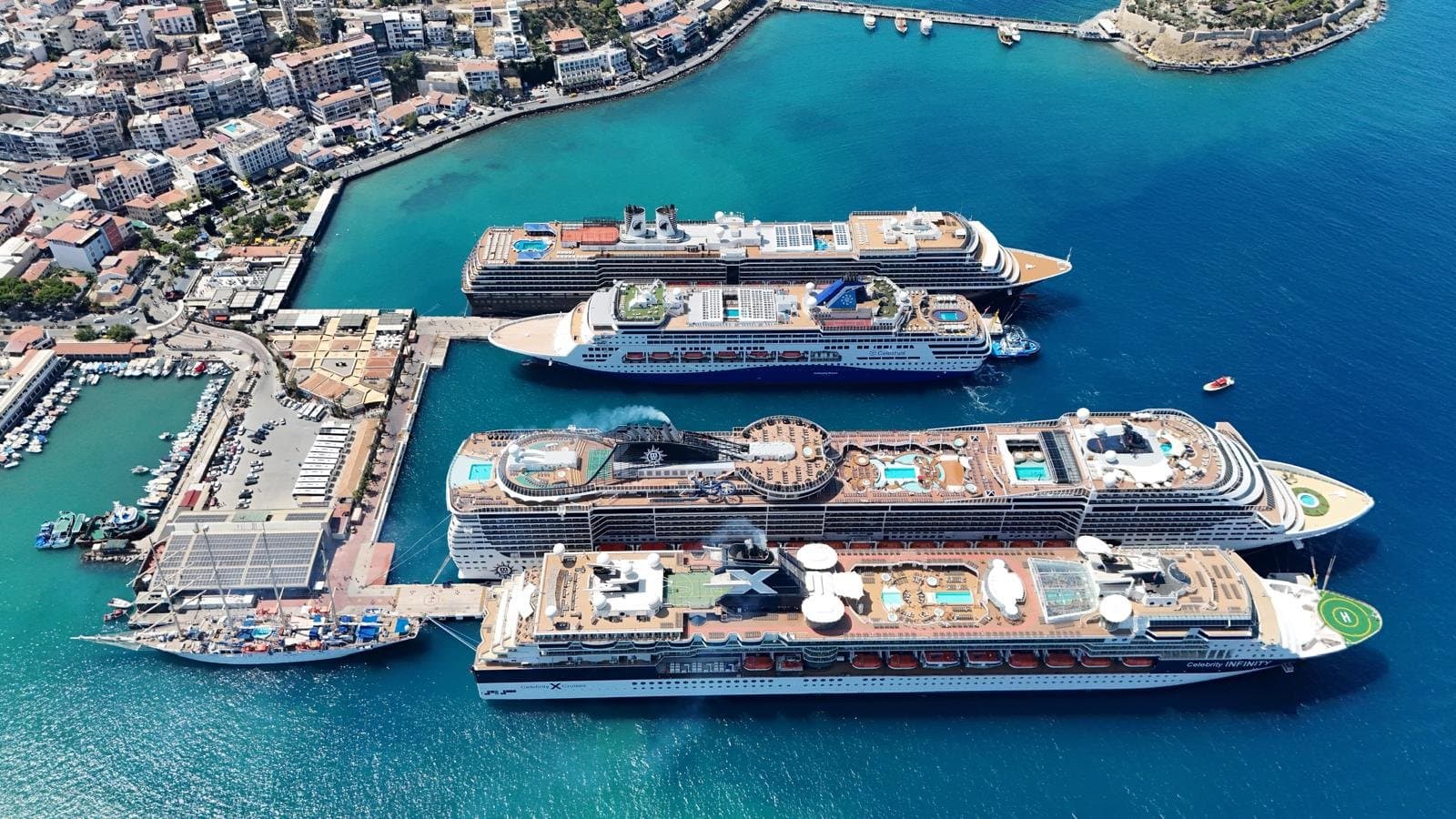 Four cruise ships berthed at Ege Port in Kuşadası on a busy summer morning, seen from the hills above the bay