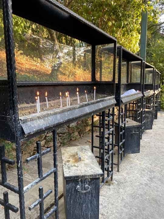 Candle stands at the House of the Virgin Mary with thin white candles burning behind glass