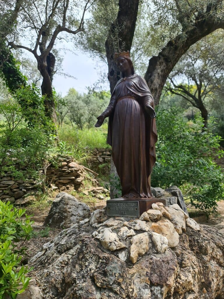 Statue of the Virgin Mary standing on a rock among olive trees on Mount Koressos